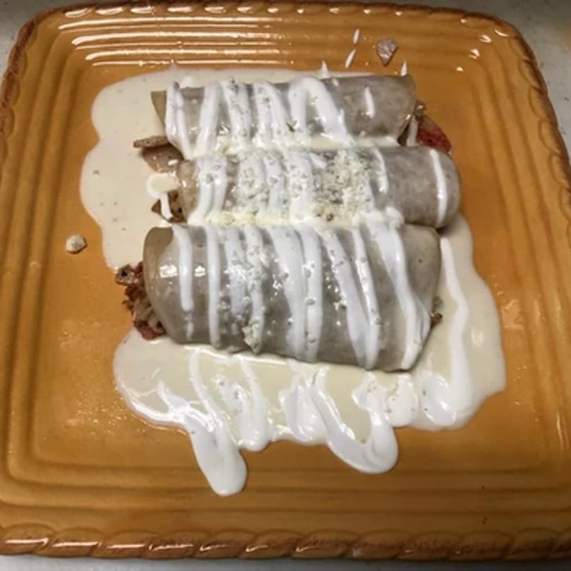 Three Si Señor 2 enchiladas covered in white sauce and crumbled cheese on a brown plate.